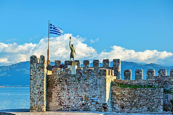 Het havenkasteel van Nafpaktos, met het standbeeld van Georgios Anemogiannis, een held van de Griekse Onafhankelijkheidsoorlog (1821), en een wapperende Griekse vlag, in de stad Nafpaktos